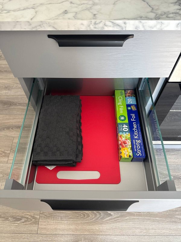 Open kitchen drawer containing cutting boards, kitchen towels and boxed food items