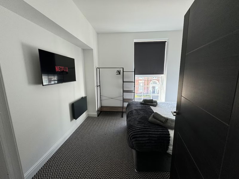 Hallway with wall-mounted TV, black sofa, carpet flooring and white walls