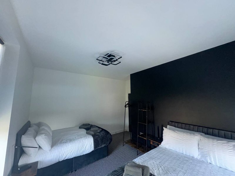 Bedroom with two beds, white bedding, dark accent wall, and ceiling light fixture