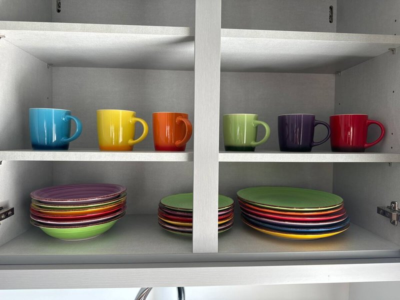 Open kitchen cabinet with colorful ceramic mugs and stacked plates in various colors