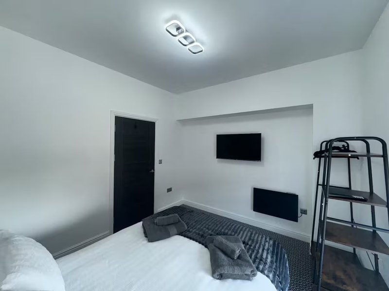 Modern bedroom with single bed, wall-mounted TV, metal frame bed, and ceiling light