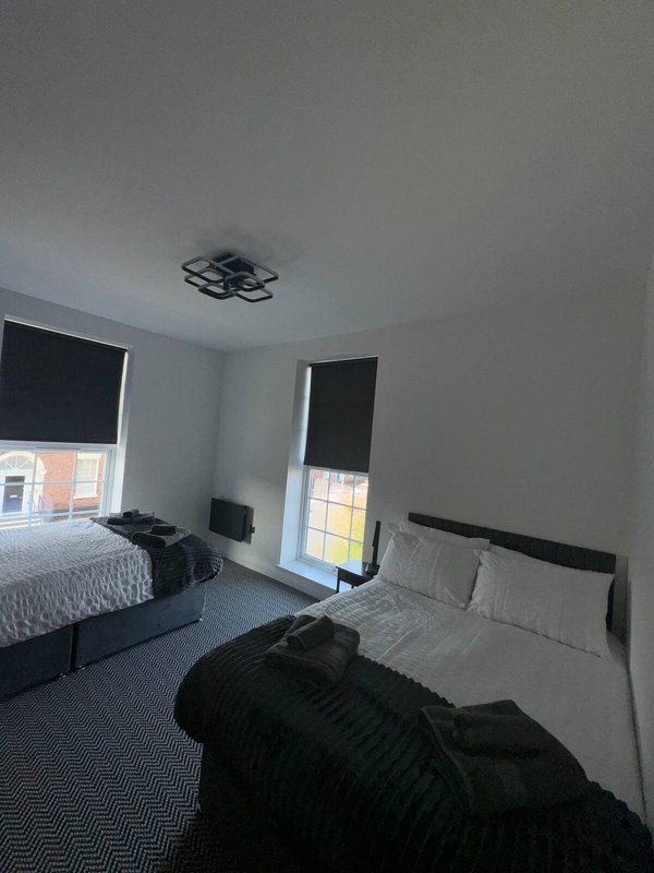 Bedroom with two beds, black bedding, ceiling fan and windows with dark blinds