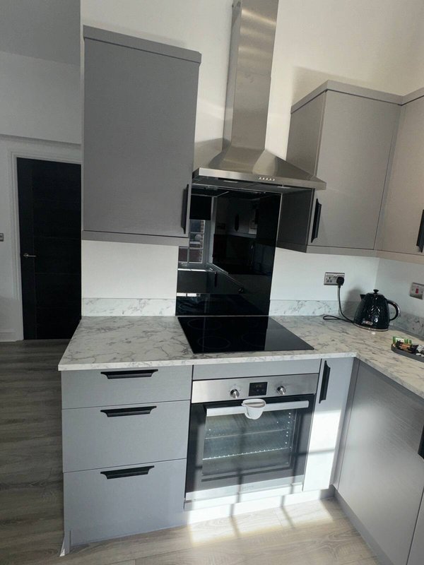 Modern kitchen with white cabinetry, black cooktop, stainless steel extractor hood and integrated oven