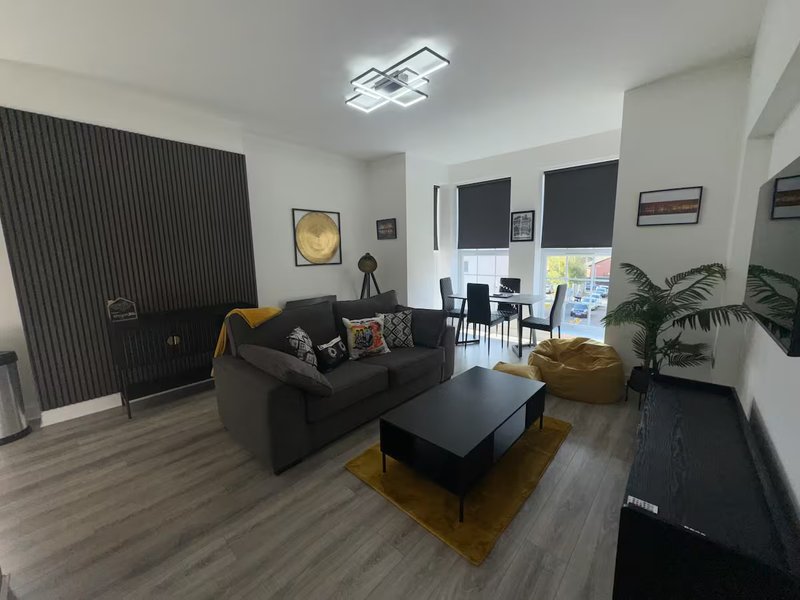 Modern living room with black sofa, coffee table, wooden flooring, and potted plant