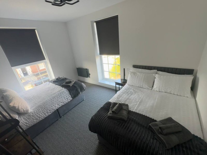 Bright bedroom with two single beds, dark roller blinds, white walls and carpet flooring