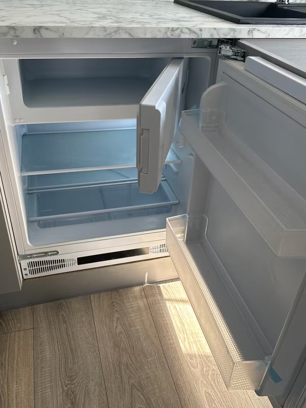 Open empty refrigerator with blue shelving in kitchen with wooden flooring
