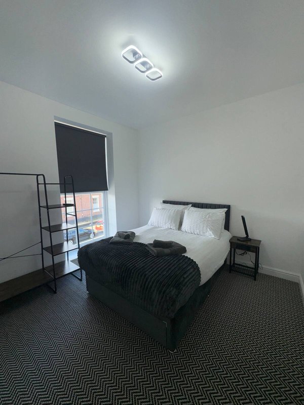 Bedroom with single bed, black throw blanket, bedside table, and window with blind