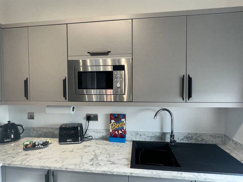 Modern kitchen with white cabinetry, stainless steel microwave, marble countertop and black sink