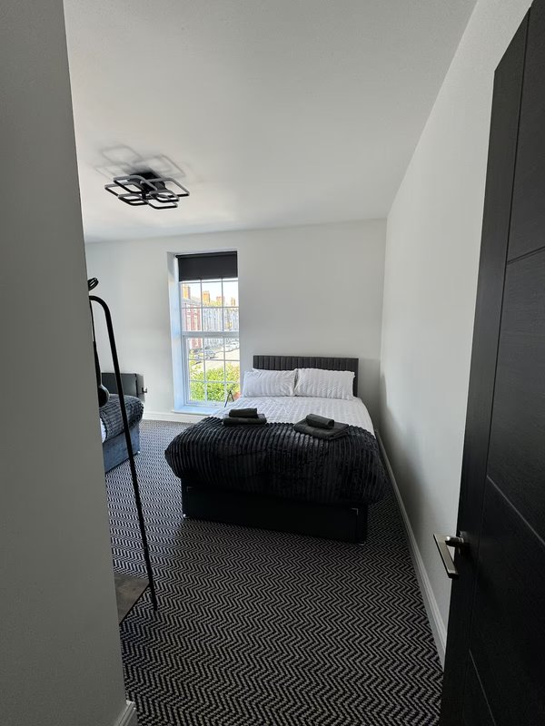 Narrow bedroom with single bed, black bedding, ceiling light, window with city view