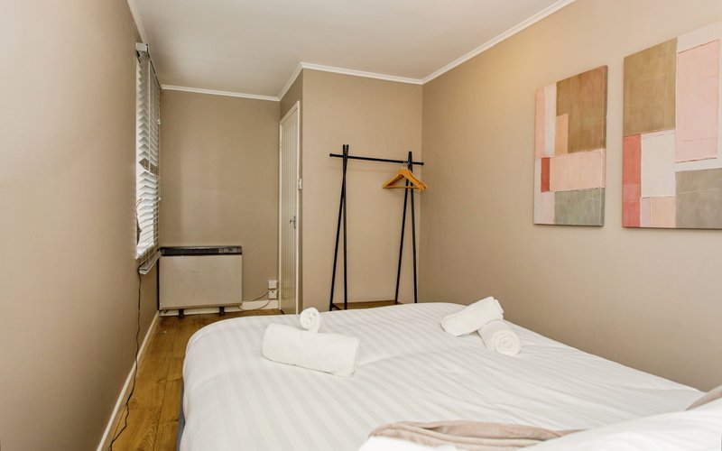 Bedroom with double bed, white linens, wooden floor, and abstract wall art