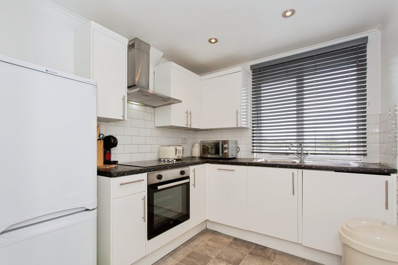 Modern white kitchen with black countertop, built-in appliances and window blinds