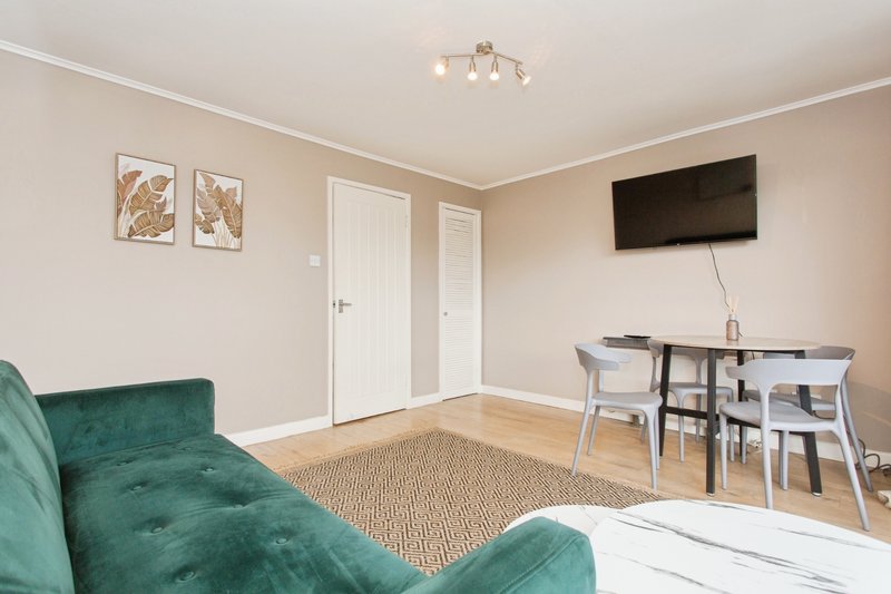 Open-plan living room with green sofa, dining table, chairs and wall-mounted TV