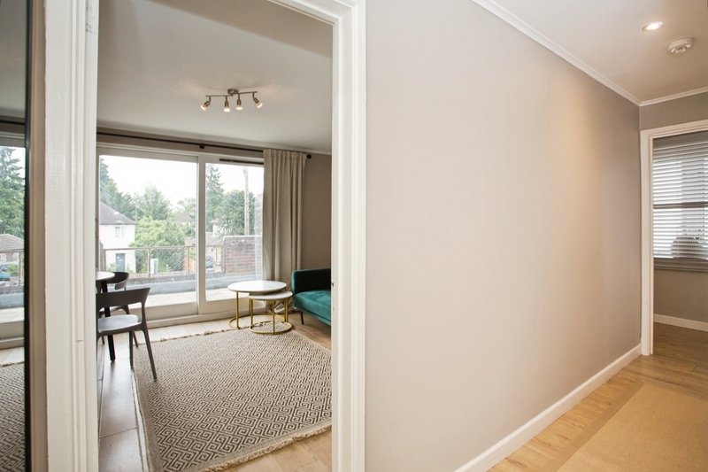 Modern hallway with wooden flooring, beige walls, and open doorway to furnished sitting area with desk and seating