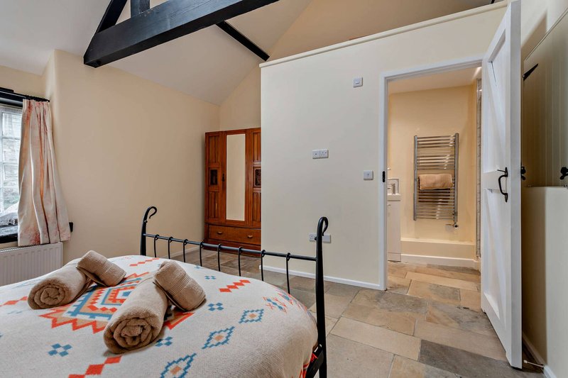 Bedroom with metal-frame bed, patterned bedding, rolled cushions, wooden wardrobe and ensuite bathroom