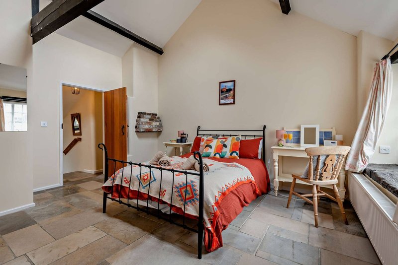 Bright bedroom with metal-frame bed, red bedding, desk, chair and wooden door entrance