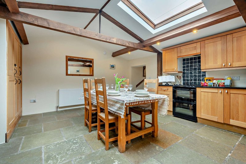 Open-plan kitchen and dining area with wooden beams, island table, and natural skylights