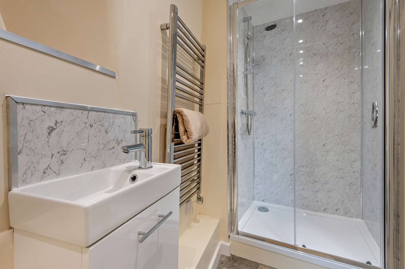 Modern bathroom with white sink, marble backsplash, heated towel rail and glass shower enclosure