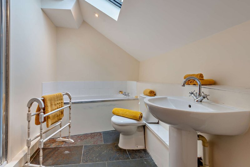 Modern bathroom with curved sink, freestanding bathtub, heated towel rail, and skylight