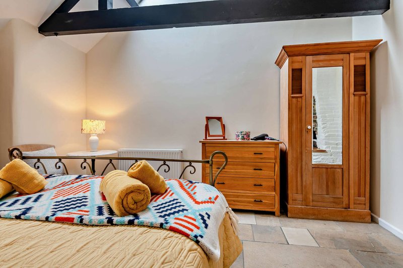Bedroom with double bed, wooden wardrobe, chest of drawers, bedside lamp and decorative pillows