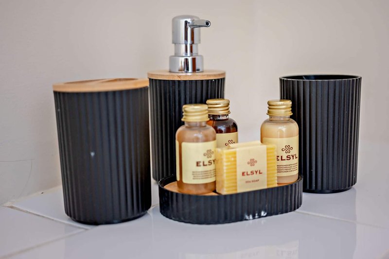 Bathroom accessories set with black ribbed containers, soap dispenser, and decorative bottled products on white surface