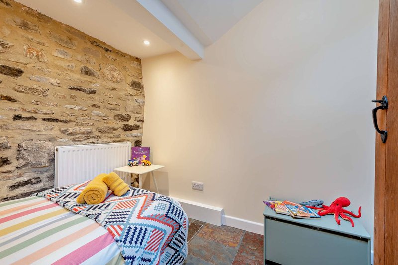 Child's bedroom with colorful striped bedding, stone feature wall, wooden beams and storage chest