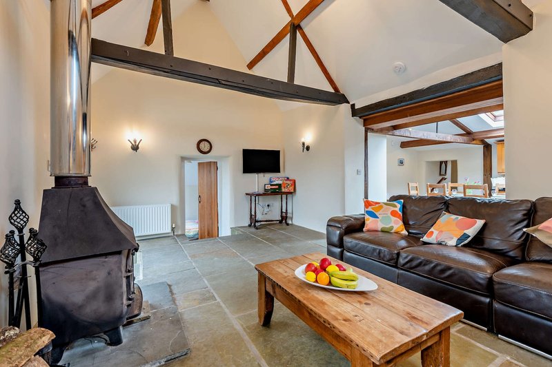 Open-plan living room with exposed beams, wood stove, leather sofa and wooden coffee table