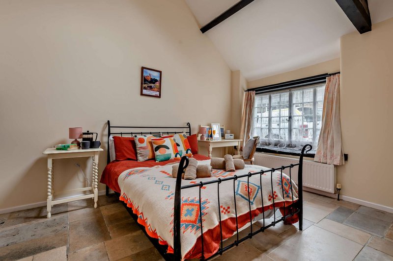 Bright bedroom with metal-frame bed, red bedding, wooden desk, and large window with natural light