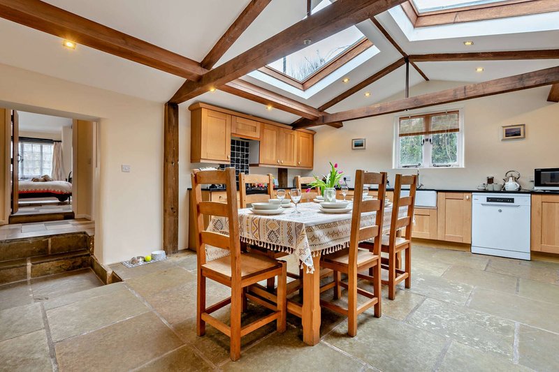 Open-plan kitchen and dining area with wooden beams, skylight, dining table and chairs