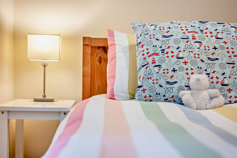 Bedroom with single bed, striped duvet, patterned headboard, desk lamp and wooden wardrobe