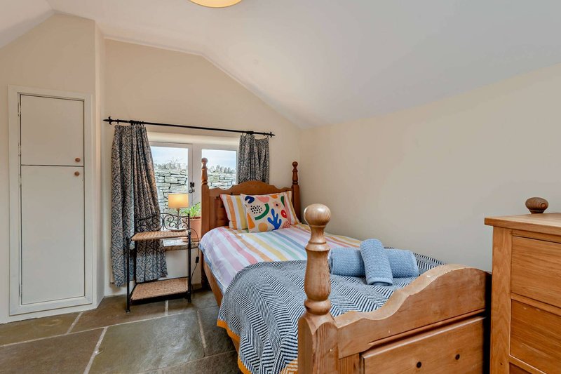 Bright attic bedroom with wooden bed, blue striped bedding, window with countryside view