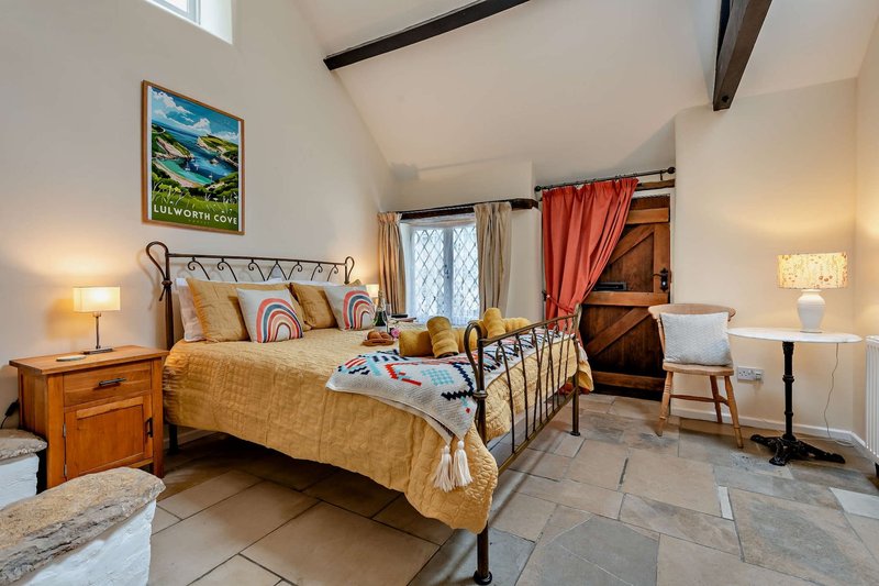 Spacious bedroom with metal-framed bed, wooden nightstand, colorful cushions, and framed landscape artwork