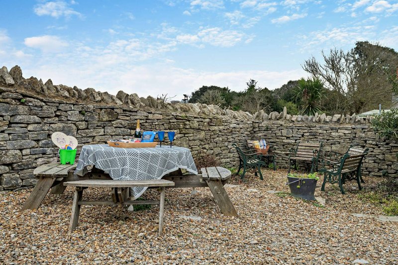 Outdoor garden seating area with picnic table, stone wall backdrop, and scattered decorative items