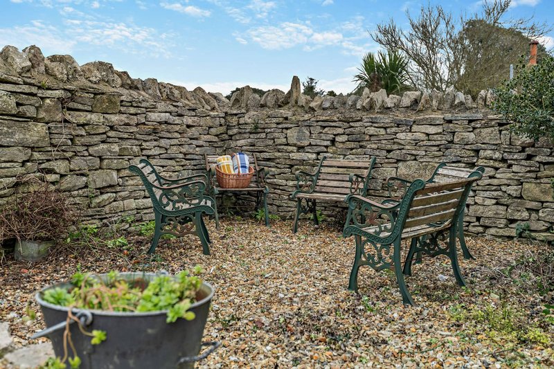 Stone-walled garden seating area with green chairs, small table, and potted plants