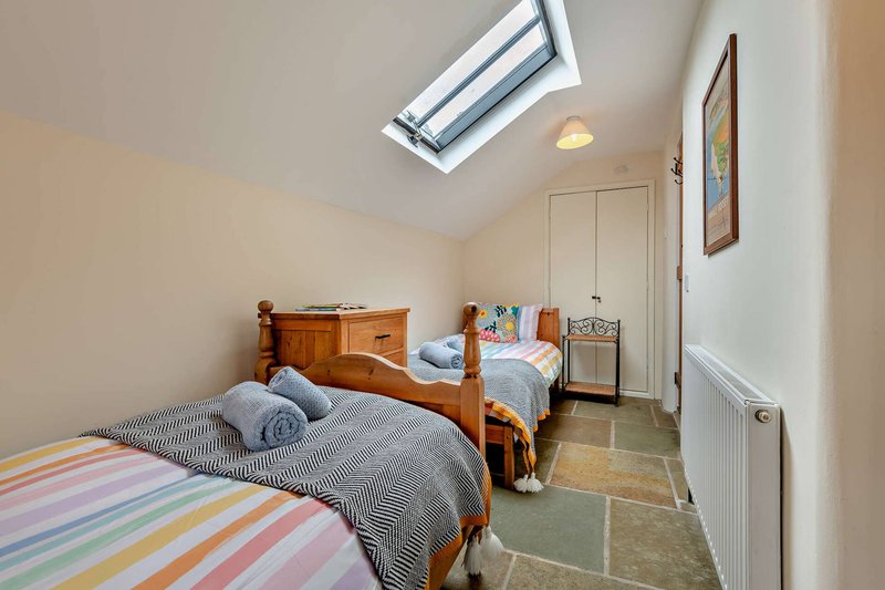 Bright attic bedroom with two single beds, wooden frames, skylight window and storage cupboard