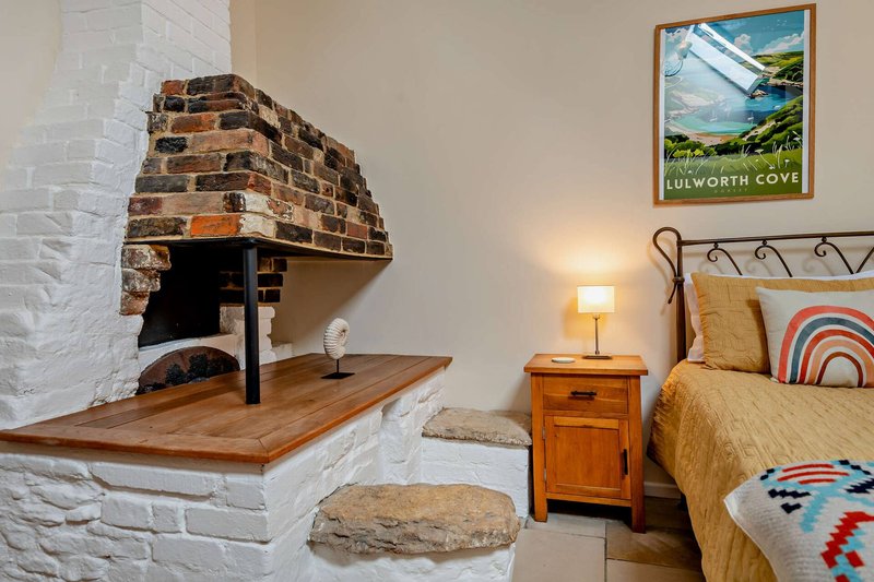 Bedroom with fireplace, single bed, wooden nightstand, and coastal landscape wall art