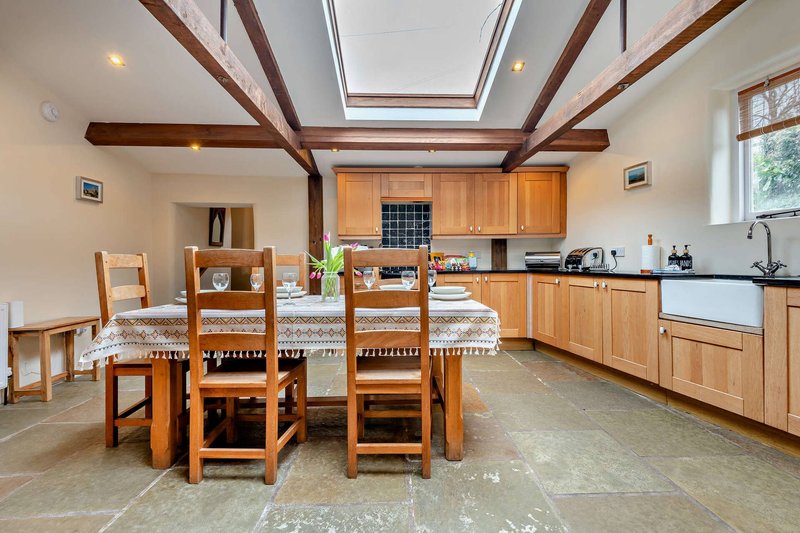 Open-plan kitchen and dining area with wooden beams, dining table, chairs, and fitted wooden cabinetry
