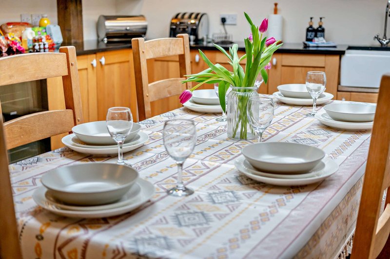 Kitchen dining area with wooden table set for meal, fresh flowers in vase, and modern appliances