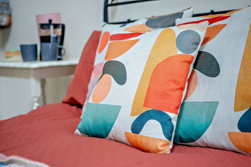 Bedroom with colorful patterned pillows on red bedding and desk with supplies
