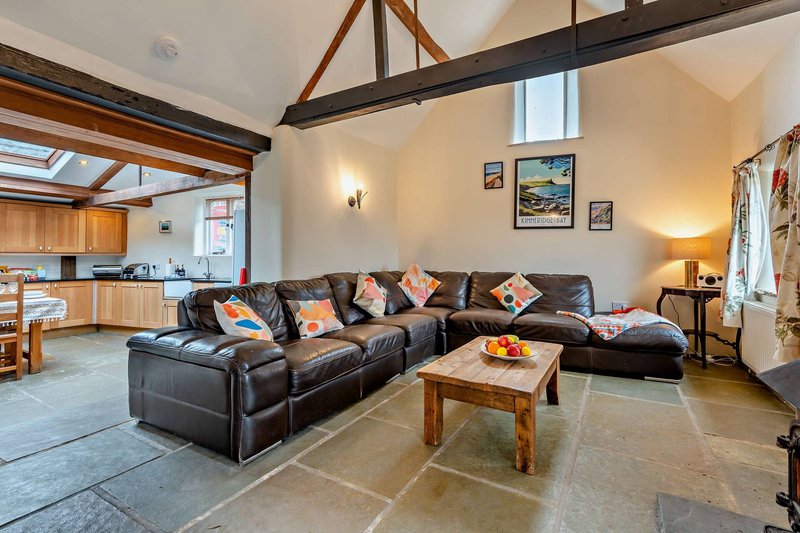Open-plan living area with black leather sectional sofa, wooden beams, and kitchen visible in background