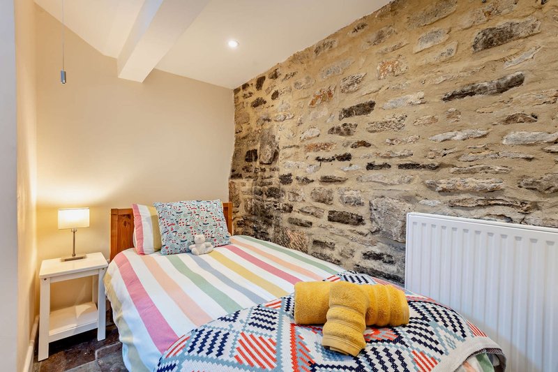 Bedroom with single bed, colorful striped bedding, stone feature wall and bedside lamp