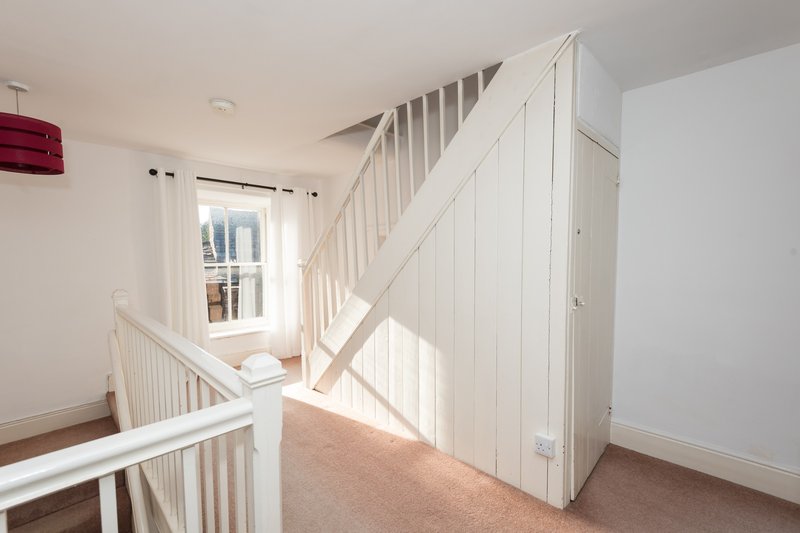 Bright staircase landing with white railings, carpeted floor, and natural light from window