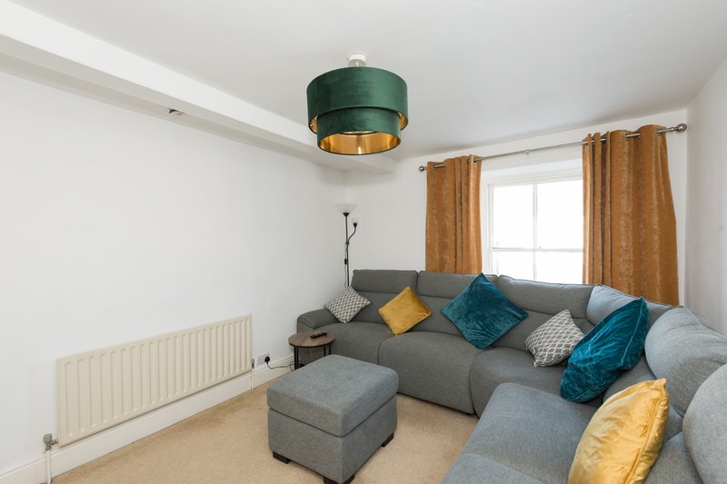 Bright living room with gray modular sofa, colorful cushions, green ceiling lamp, and window with gold curtains