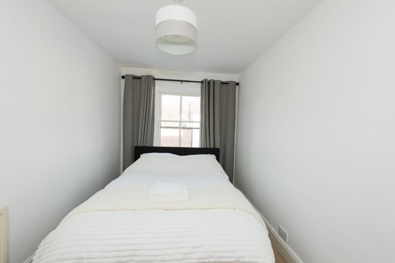 Narrow bedroom with single bed, gray curtains, window and ceiling light fixture