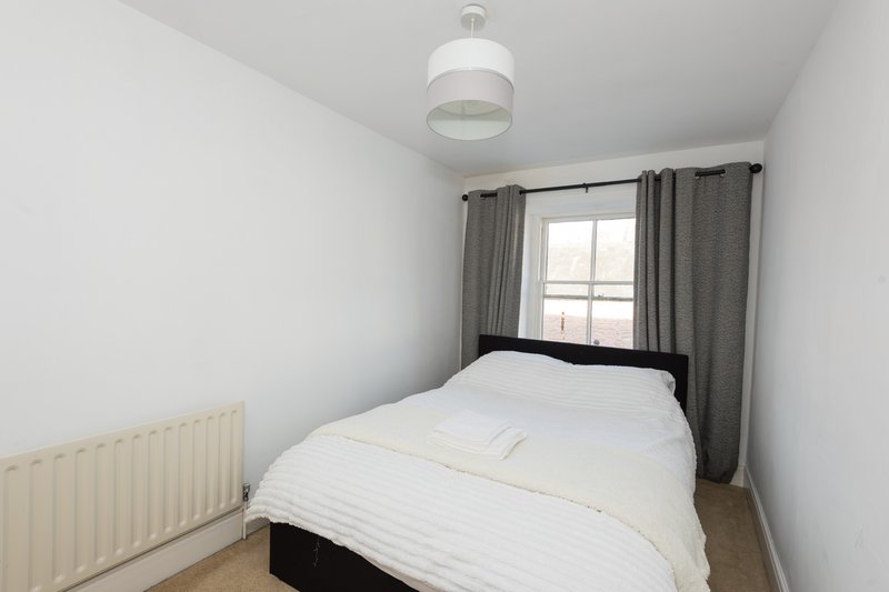 Modest bedroom with double bed, white bedding, grey curtains, radiator and pendant light