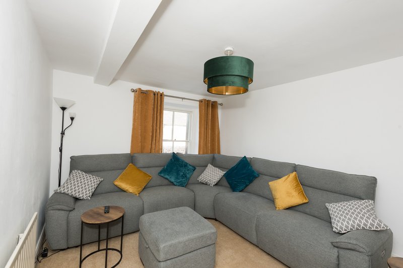 Modern living room with gray sectional sofa, colorful cushions, wooden side table, and green ceiling light