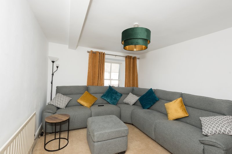 Modern living room with gray corner sofa, colorful cushions, ottoman, and pendant light