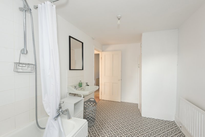 Bright bathroom with white subway tiles, shower with curtain, pedestal sink and patterned floor