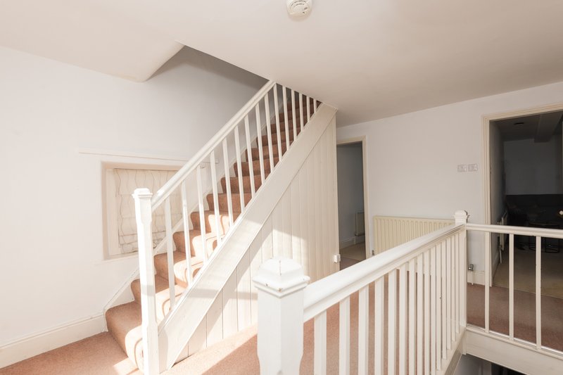Bright hallway with white staircase and landing, wooden handrails, neutral carpet