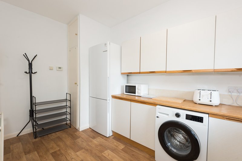 Modern kitchen with white appliances, wooden shelving, washing machine and wooden flooring