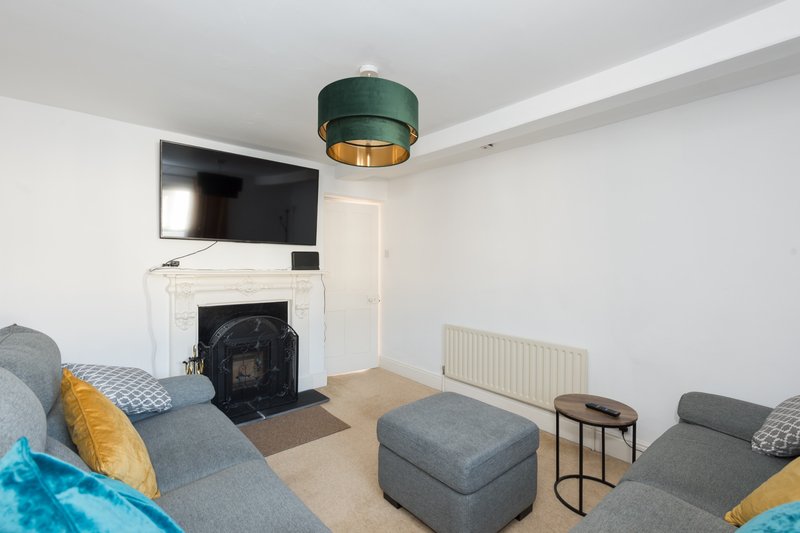 Modern living room with grey sofas, fireplace, wall-mounted TV, and green ceiling lamp